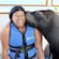 A smiling woman in a life jacket being kissed by a sea lion